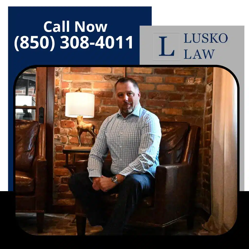 Professional portrait of an attorney sitting in a leather armchair in front of an exposed brick wall, branded for Lusko Law.