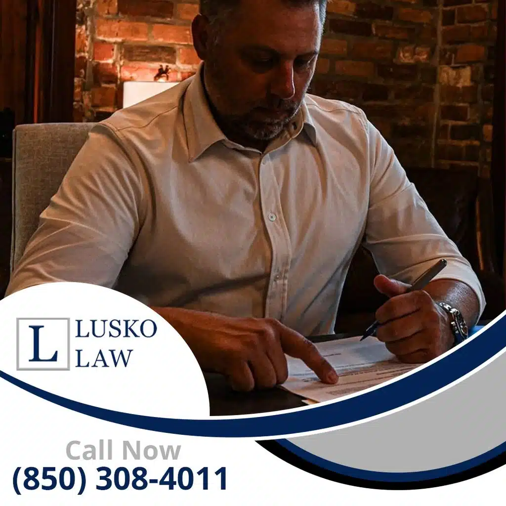 An attorney reviewing and signing legal documents at his desk in an office with an exposed brick background, branded for Lusko Law.