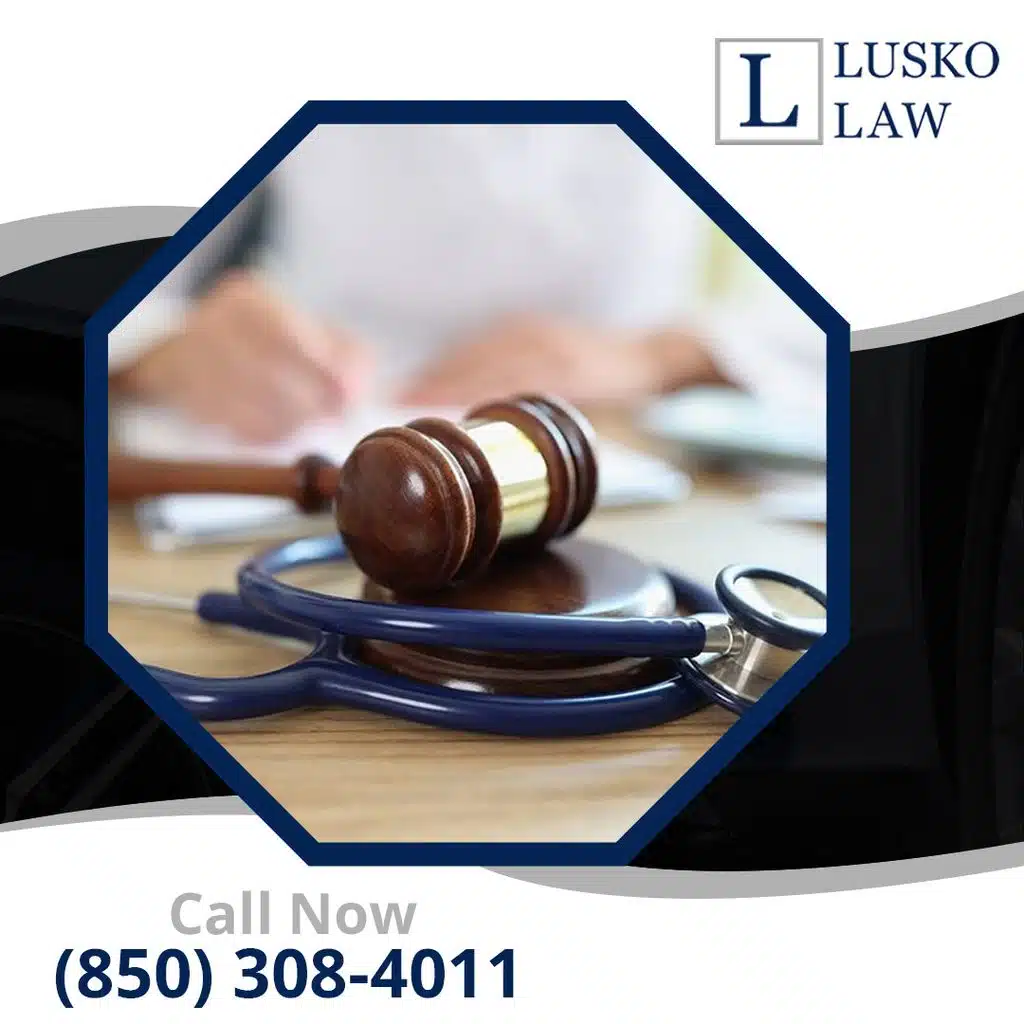 A wooden judge's gavel resting on top of a stethoscope on a desk with a legal professional reviewing documents in the background, branded for Lusko Law.